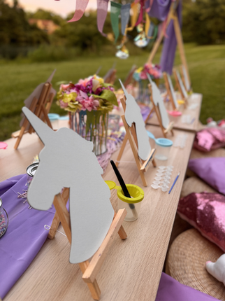 Unicorn cutouts on easels for an outdoor painting party with colorful decorations.