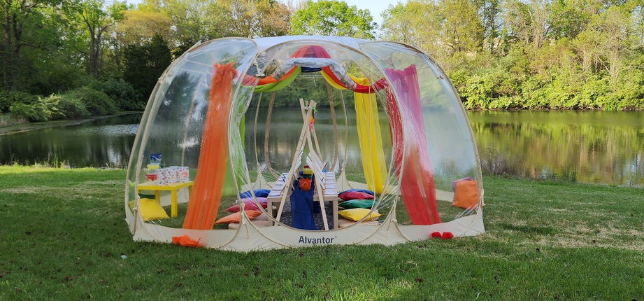 Clear BubbleTent with colorful interior decorations outdoors by a lake.