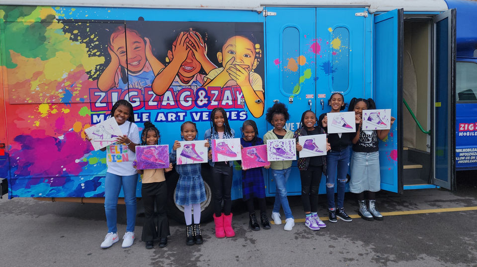 Girls display artwork before 'ZIG ZAG & ZAY MOBILE ART VEHICLE'.