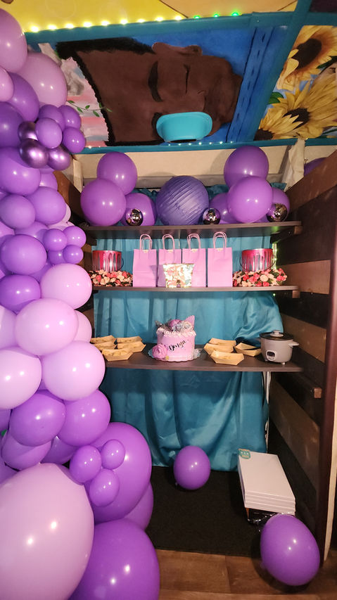 Purple balloons garland with pink decorations and cake on shelves.