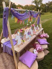 Outdoor unicorn picnic table with purple drapes, cushions, and colorful bunting.