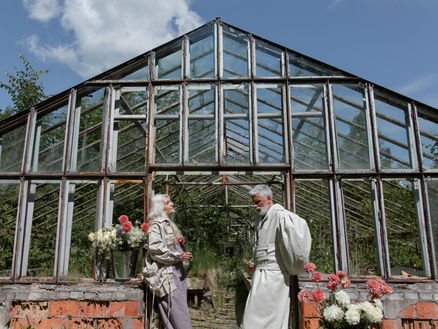 An elderly couple standing and leaning on a greenhouse doorway