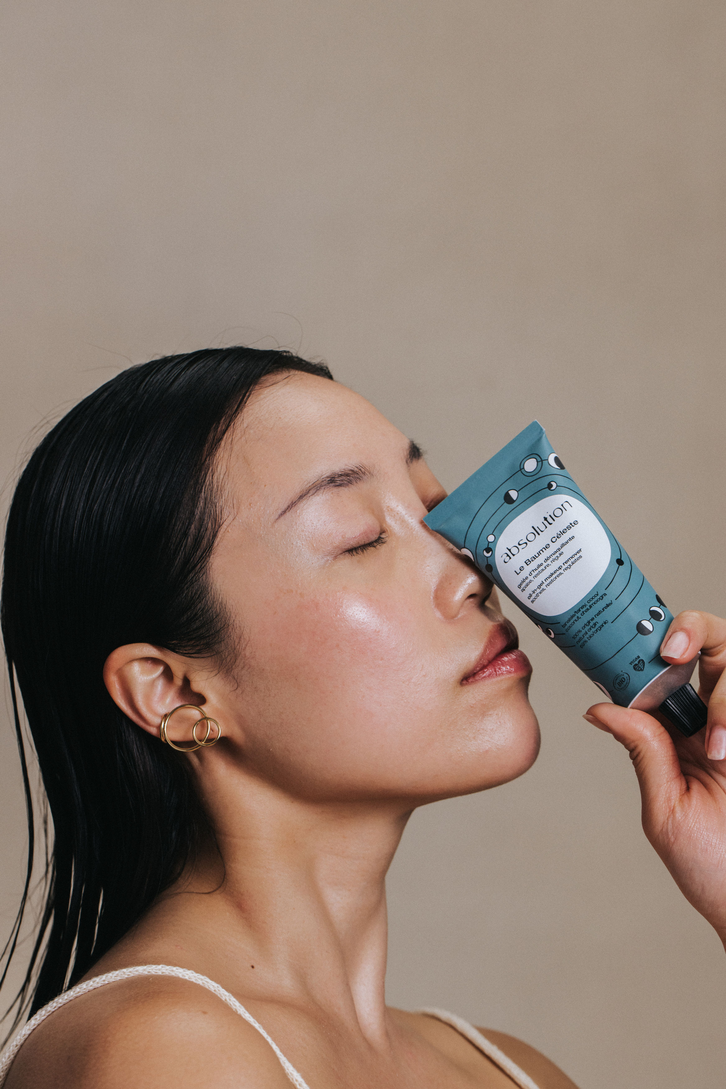 Model drži Absolution Le Baume Céleste balzam za skidanje šminke uz blistavu kožu i elegantnu skincare estetiku.