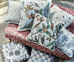 Made to measure cushions in floral and botanical fabrics, styled on a red upholstered bench in a home interior.