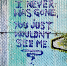 Photographed graffiti message on light blues and gray corrugated metal wall covered with a chainlink fence reads: "I never was gone, you just wouldn't see me.”