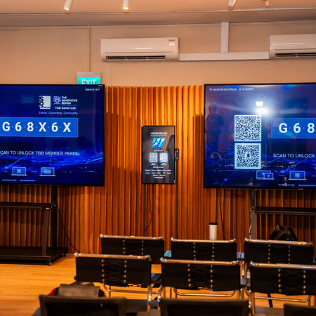 Conference room at the Think Global, Act Local event with two large screens displaying 'The Generative Beings' and 'G68X6X' and QR codes.