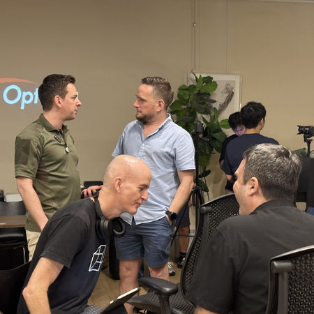 Small group talks beside a projection screen during The Stage: Demo Day 3 at SQ Collective.