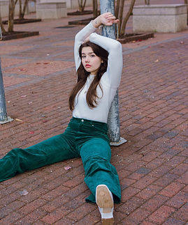 A girl is sitting on the ground and leaning against a lamppost with her arms above her head.