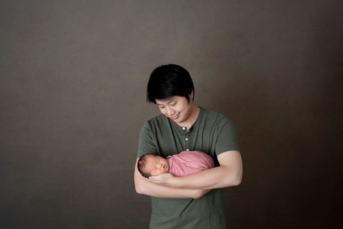 A dad is holidng his newborn baby girl, swaddle in a pink wrap
