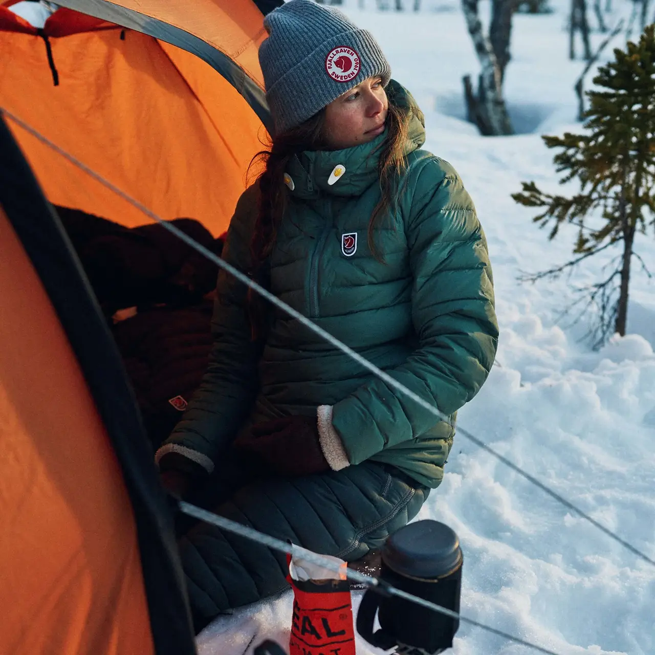 a lady in a fjallraven coat going into a tent in the snow