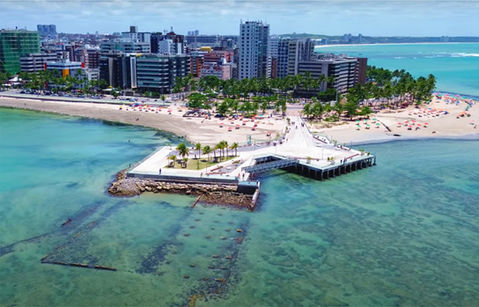Vista aérea panorâmica da deslumbrante orla de Maceió, Alagoas, com águas cristalinas, praias de areia branca, coqueiros e o icônico Marco dos Corais. Representa o cenário paradisíaco da 10 Milhas de Alagoas.