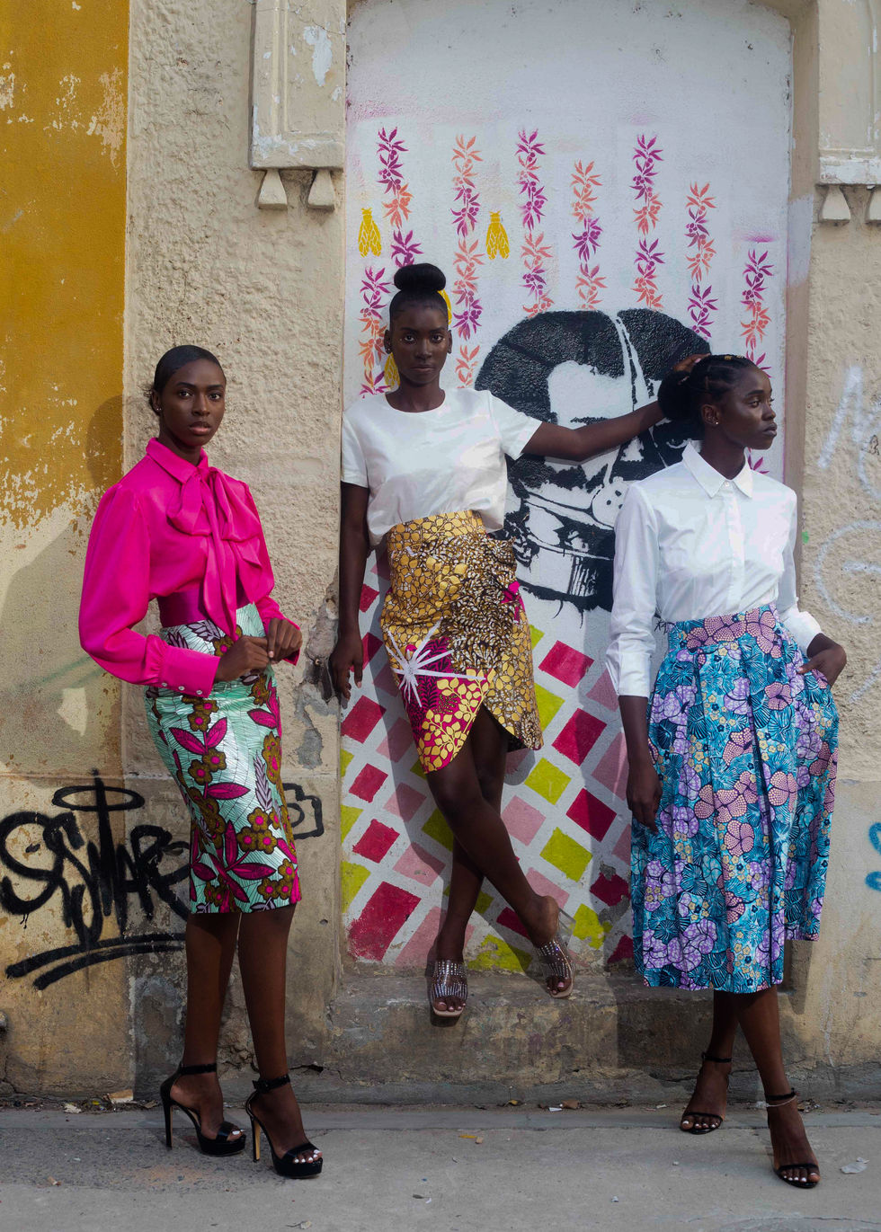3 outfits: a silk pink blouse with a big bow and with a mint african printed pencil skirt. A white silk crop top with a gold african printed drapped skirt. A white cotton shirt with a blue african printed midi skirt.