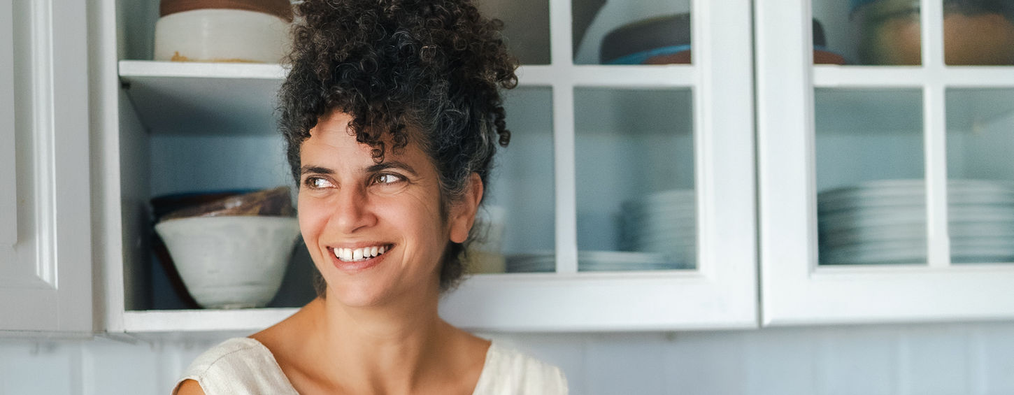 אישה יושבת על השיש מחייכת, ארונות לבנים, פירות, ליהי בסדר.