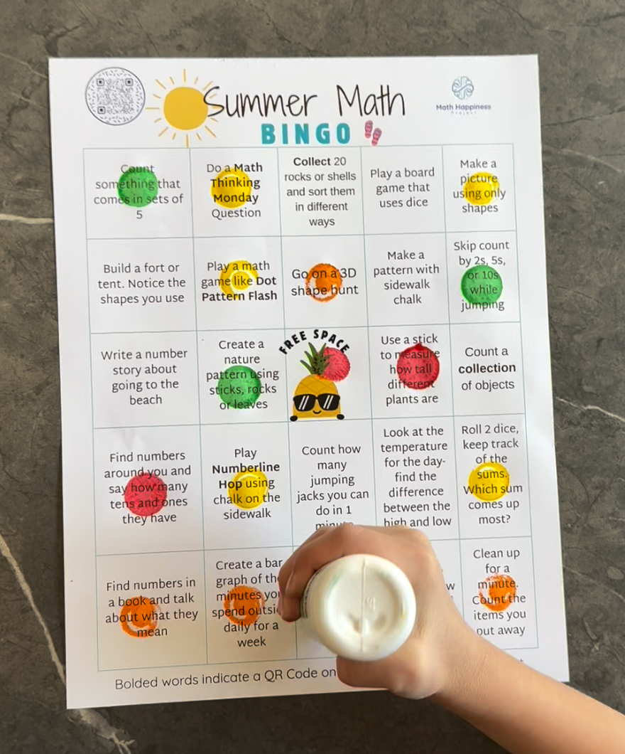 a child's hand uses a bingo marker to stamp a summer math bingo card. Various squares on the card are already stamped with different colors