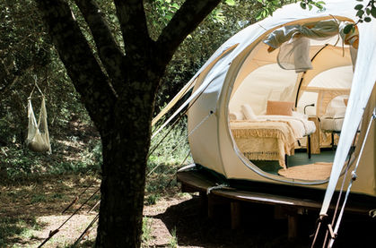 two single beds inside a Glampling tent placed in a forest next to a hammock 
