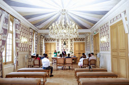 Photographie de la cérémonie de mariage civil d’Olivier et Chamima dans la salle des mariages de la mairie de Levallois-Perret. On y découvre les mariés et leurs proches face à l’élu, sous un lustre majestueux et une décoration raffinée. Photographe de mariage à Levallois-Perret et en région parisienne, je capture avec discrétion et authenticité les moments forts de la cérémonie civile, afin d’immortaliser vos souvenirs dans un cadre élégant et lumineux.