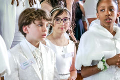 Portrait d’Emma, fillette en robe blanche et couronne perlée, au milieu d’un groupe d’enfants pendant leur première communion. Elle est au centre de la composition, avec ses lunettes violettes et ses tresses, regardant droit vers l’objectif. Cette photo a été prise à la Paroisse Notre-Dame du Sacré-Cœur de Coeuilly lors d’une cérémonie de première communion. Photographe de cérémonies religieuses et d’événements familiaux, je réalise des reportages sensibles en église à Gentilly et dans toute la région parisienne.