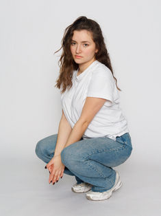 Polas comédienne en studio fond blanc, pose accroupie 3/4. Séance professionnelle en Île-de-France pour mise à jour book et agence artistique.