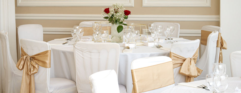 Table de mariage décorée en blanc et or, avec chaises recouvertes de housses blanches et nœuds dorés, vaisselle et composition florale, photo de mariage à Saint-Gratien par Colombe Photographie.