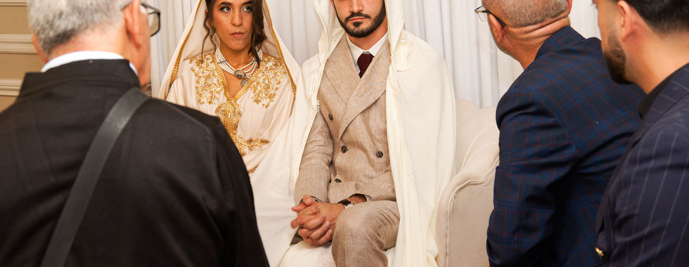 Mariés assis en tenue traditionnelle kurde-tunisienne pendant la cérémonie religieuse de leur mariage, entourés de leurs proches, photo capturée par Colombe Photographie à Saint-Gratien.