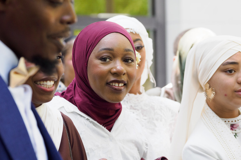 Portrait d’invitée en hijab bordeaux entourée d’amis et de la mariée lors du mariage civil de Malika et Richard à Guyancourt, en Île-de-France. Reportage mariage naturel et lumineux réalisé par Colombe Delons, photographe de mariage en région parisienne.