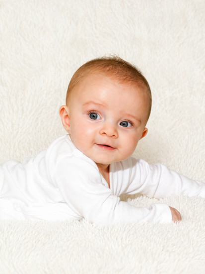 Photo de bébé allongé sur le ventre regardant l’objectif, réalisée en studio photo à Gentilly. Fond blanc épuré et lumière naturelle pour un rendu professionnel, idéal pour un book bébé ou des souvenirs en Île-de-France.