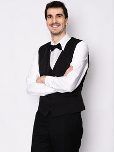 Pola de Raphaël Distler Stragier, comédien, en plan américain de trois quarts. Il pose avec les bras croisés, affichant un sourire naturel. Vêtu d'un pantalon, d'un gilet et d'un nœud papillon noir sur une chemise blanche, il incarne une élégance classique. Photo réalisée en studio sur fond blanc, sans retouche, idéale pour les agences et castings recherchant des profils authentiques et expressifs.