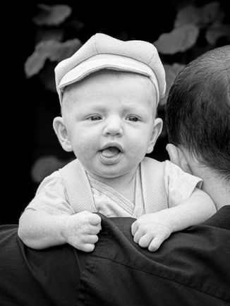 Portrait en noir et blanc d’un bébé installé sur l’épaule de son parent, photographié en extérieur lors d’une séance bébé en région parisienne. Le bébé regarde l’objectif avec une expression curieuse et spontanée. Photographe nouveau-né et bébé à Gentilly, proposant des portraits authentiques et naturels en studio ou en extérieur.