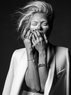 Alexia dans un costume blanc, mains sur la bouche, yeux fermés, cheveux dans le vent, maquillage créatif, fond noir.