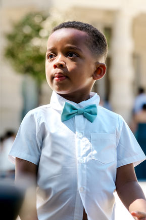 Portrait d’un jeune garçon d’honneur lors d’un mariage à Dammarie-lès-Lys, vêtu d’une chemise blanche et d’un nœud papillon turquoise. Une photo pleine de tendresse capturée par Colombe Photographie, photographe de mariage en Île-de-France, basée à Gentilly et spécialisée dans les reportages familiaux, naturels et spontanés à Paris et en région parisienne.