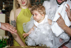 Bébé Giulia en robe blanche décorée de fleurs lors de son baptême à l’église Sainte Geneviève de Garges-lès-Gonesse. Les parents tiennent leur enfant au-dessus de la fontaine baptismale pendant que le prêtre verse l’eau bénite. Reportage réalisé par une photographe baptême à Paris et en Île-de-France, capturant l’émotion de la cérémonie familiale.