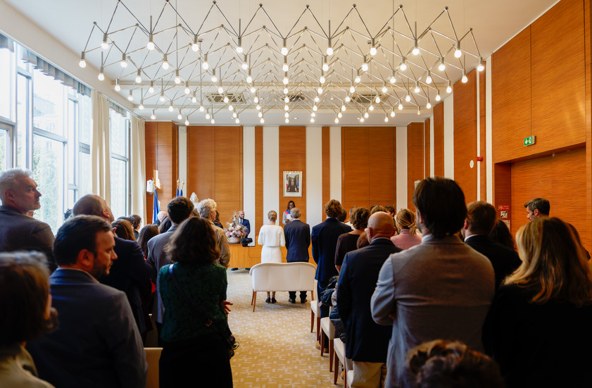 Vue d’ensemble de la salle des mariages de la mairie du 17e arrondissement de Paris pendant la cérémonie civile de Xavier et Camille, entourés de leurs invités. Reportage réalisé par Henock pour le studio Colombe Photographie, photographe de mariage civil à Paris et en Île-de-France.