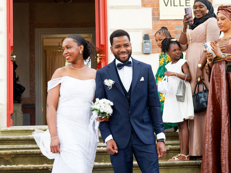 Photographie de mariage civil de Sékou et Mariama à la sortie de la mairie de Dammarie-lès-Lys, en Seine-et-Marne. Les mariés se tiennent main dans la main, tout sourire, entourés de leurs proches. Cette image chaleureuse et spontanée illustre l'émotion des instants partagés juste après la cérémonie. Reportage réalisé par Colombe Photographie, photographe de mariage à Gentilly et en région parisienne, spécialisée dans les mariages civils et les cérémonies en petit comité.