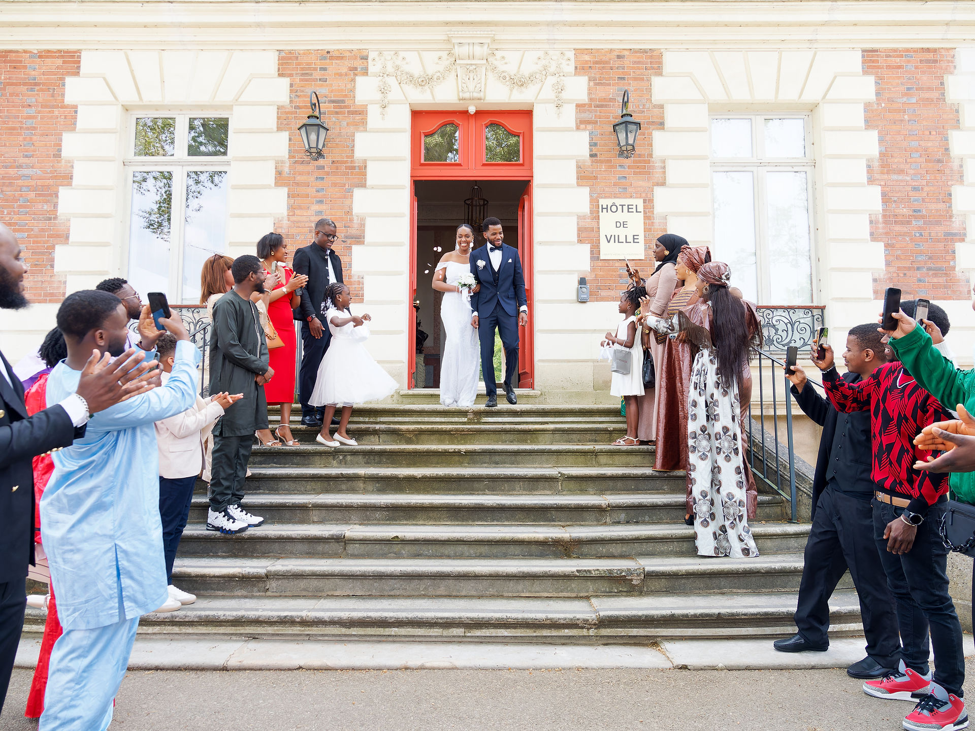 Photo de mariage civil de Sékou et Mariama à Dammarie-lès-Lys, à leur sortie de la mairie sous les applaudissements de leurs proches. Les mariés, élégants et rayonnants, descendent les marches main dans la main tandis que les invités les acclament et les prennent en photo. Ce reportage a été réalisé par Colombe Photographie, photographe de mariage basée à Gentilly, spécialisée dans les cérémonies civiles et familiales en région parisienne et en Île-de-France.