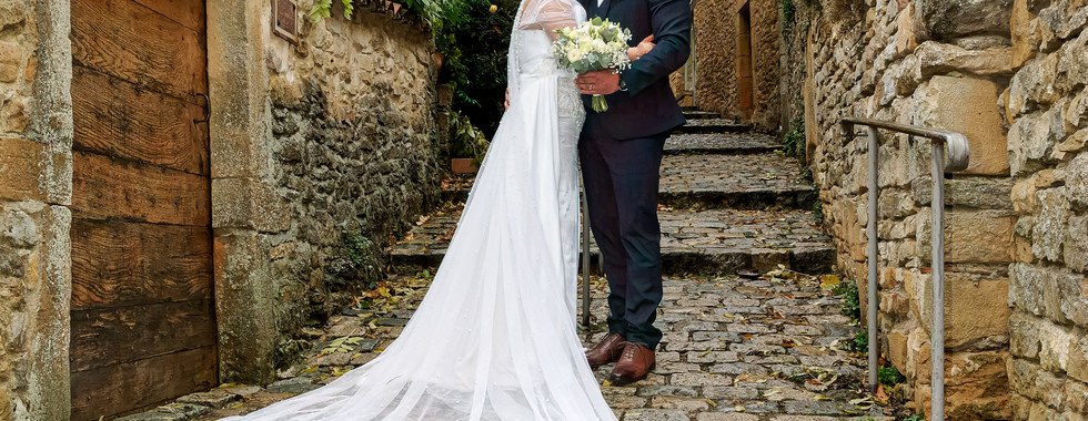 Photographie de mariage de Rania et Jordan enlacés dans une ruelle pavée, la mariée portant une longue traîne perlée. Photo réalisée par Colombe Photographie, photographe de mariage à Lyon.