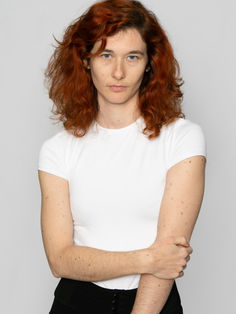 Pola de Romane Renaud, modèle, réalisée en studio sur fond blanc, sans retouches de peau, pour un rendu naturel et authentique. Le plan américain présente Romane de face, une main tenant son bras, avec une expression neutre qui apporte une touche de sérénité. Ce pola simple et élégant est parfait pour les portfolios de mannequins, modèles et comédiens, ainsi que pour les directeurs de casting et agences à la recherche d'une image épurée mais pleine de présence.