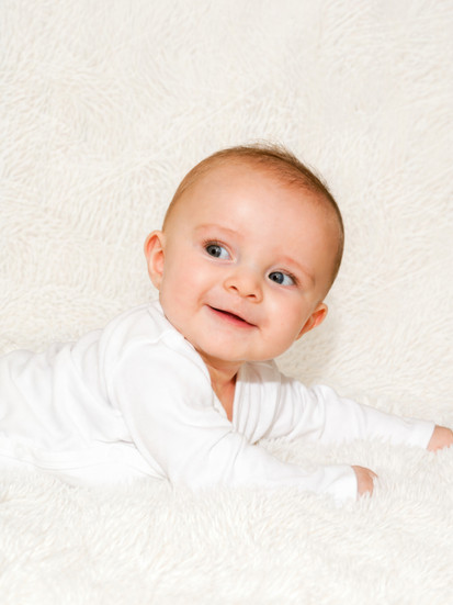 Photo de bébé allongé sur le ventre sur fond blanc, regard tourné sur le côté, réalisée en studio photo à Gentilly en Île-de-France. Portrait naturel et lumineux idéal pour un book bébé ou des photos souvenirs professionnelles.