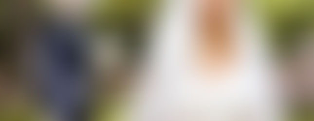 Photo de mariage d’Omer et Syrine en région parisienne : la mariée en robe blanche et voile dentelé, ceinte d’un ruban rouge, se tient au premier plan tandis que le marié s’avance derrière elle, un bouquet à la main.