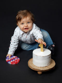 Portrait d’enfant réalisé au Studio Colombe Photographie à Gentilly, en région parisienne, lors d’une séance photo spéciale premier anniversaire. L’image montre un bébé jouant près d’un petit gâteau décoré d’un chiffre « 1 », idéal pour illustrer une séance smash the cake ou une séance anniversaire en studio. Notre studio spécialisé en photographie enfant et famille propose des portraits naturels, expressifs et chaleureux, en studio à Gentilly ou partout en Île-de-France.