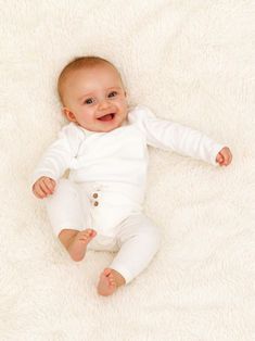 Bébé allongé sur fond blanc en moumoute, regard caméra et sourire spontané. Séance photo bébé réalisée en studio à Gentilly, proche Paris, par un photographe spécialisé en portraits bébé et famille en Île-de-France. Mise en valeur de l’expression naturelle et de la douceur de l’enfance.
