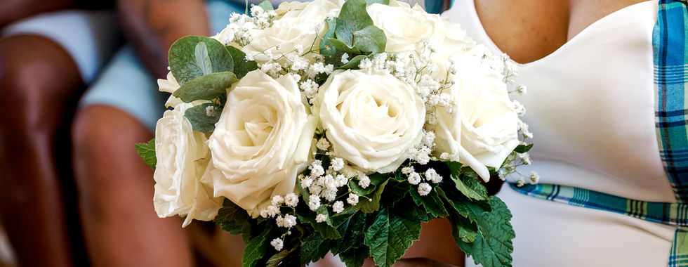 Photographie du bouquet de la mariée lors du mariage civil de Mallory & Ruddy en région parisienne. Composé de roses blanches, de gypsophile et de feuillage vert tendre, ce bouquet élégant repose sur les genoux de la mariée, vêtue d'une robe blanche avec un rappel de tartan bleu. Photo capturée par Colombe Photographie, photographe de mariage à Gentilly et dans toute l’Île-de-France, spécialisée dans les reportages sincères et lumineux.