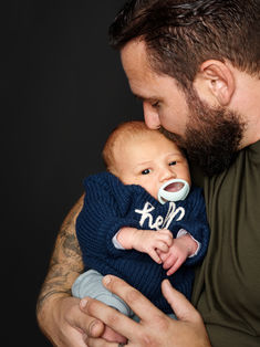 Photo naissance de Benjamin, blotti dans les bras de son père qui dépose un baiser sur son front. Le contraste entre le pull bleu marine du bébé et le fond sombre souligne la douceur du moment. Prise de vue réalisée au studio Colombe Photographie à Gentilly. Photographe naissance et famille à Paris, spécialisée dans les portraits empreints d’émotion, révélant la complicité et la tendresse des liens familiaux.