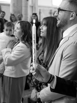 Le parrain de Samuel tient le cierge allumé, un geste symbolique de la lumière de la foi chrétienne, lors de la cérémonie de baptême. Ce moment capturé avec attention représente l'engagement spirituel du parrain à guider Samuel sur son chemin de foi, marquant l'importance de ce rôle sacré dans la communauté chrétienne.