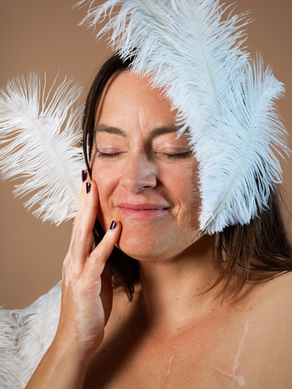 Portrait serré de Vinciane, modèle atteinte de vitiligo, les yeux fermés et entourée de plumes blanches. Son expression apaisée reflète la sérénité et l’acceptation de soi. Photo réalisée au studio Colombe Photographie à Gentilly dans le cadre d’un shooting vitiligo artistique. Photographe vitiligo à Paris spécialisée dans les portraits sensibles et la mise en valeur des peaux atypiques.