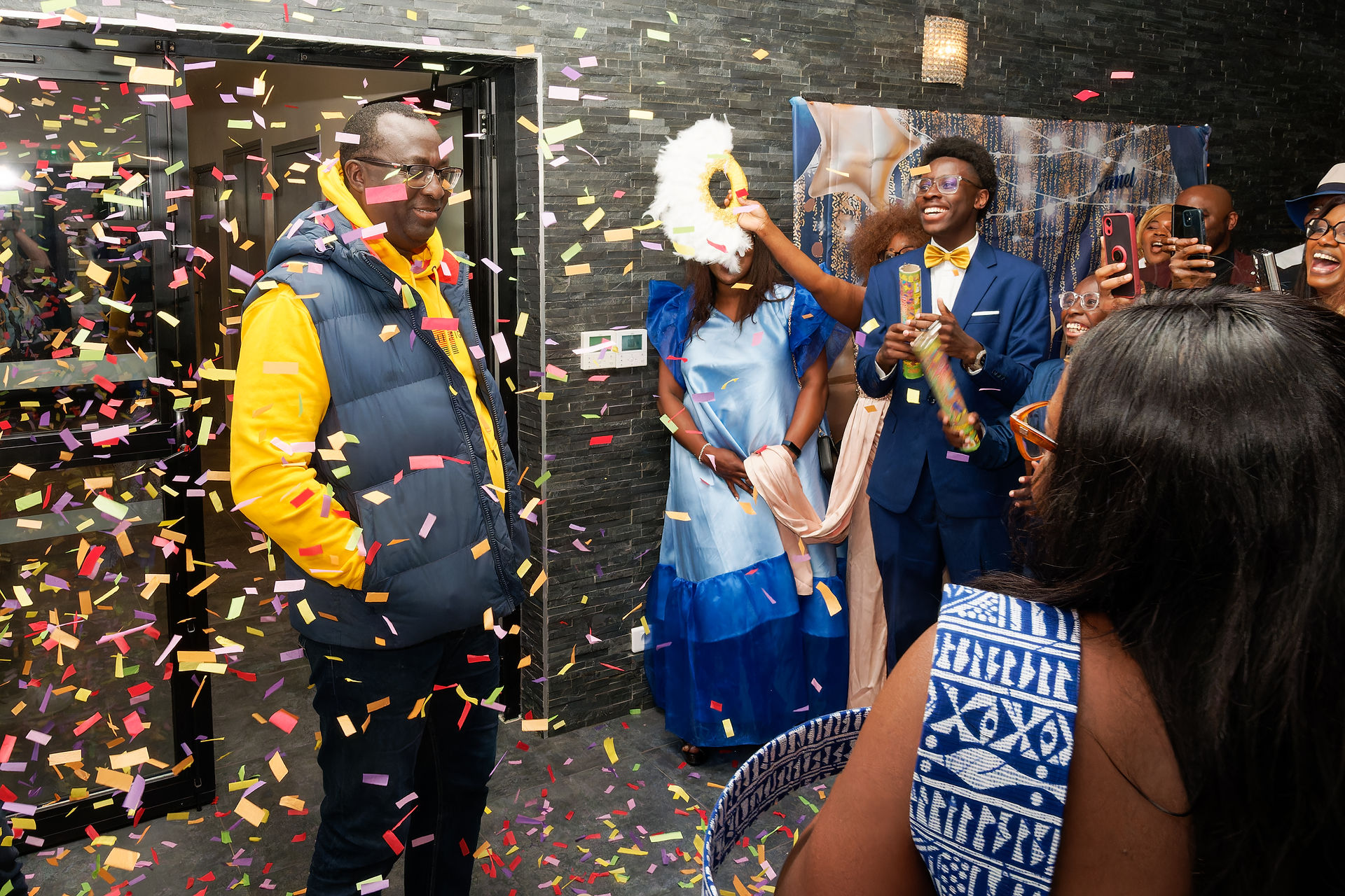 Photo de l’arrivée d’Armel lors de sa fête surprise pour ses 50 ans, accueillie par une pluie de confettis et les sourires de ses proches. Capturée en intérieur dans une salle décorée en région parisienne, cette image retranscrit la surprise, la joie et l’ambiance festive. Reportage réalisé par Colombe Photographie, photographe d’événements familiaux à Gentilly et en Île-de-France.
