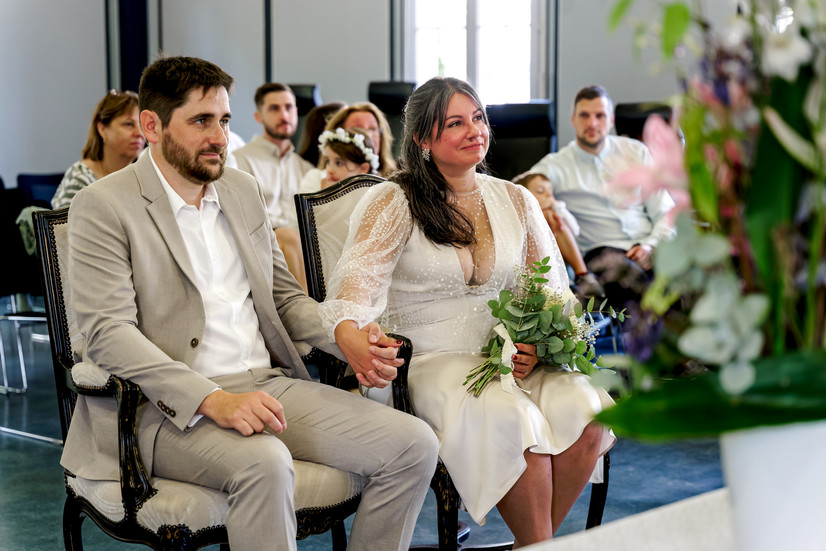 Photographie du mariage civil d’Élodie et Damien à la mairie de Palaiseau : les mariés, main dans la main, vivent un instant chargé d’émotion lors de la cérémonie. Reportage photo réalisé par Henock, photographe partenaire du Studio Colombe Photographie, spécialisé dans les mariages en Essonne et en Île-de-France.