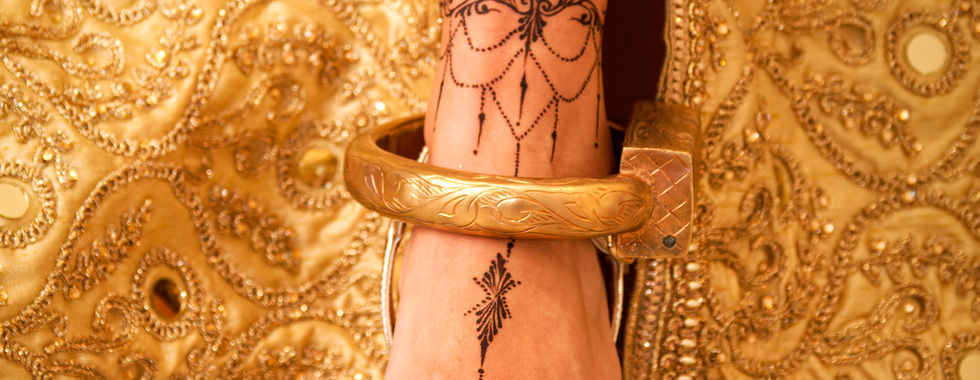Gros plan sur le pied de la mariée orné de henné et chaussé de sandales dorées assorties à la robe traditionnelle tunisienne, photo de détails par Colombe Photographie à Saint-Gratien.