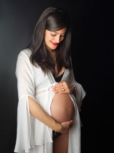 Portrait grossesse en clair-obscur avec voilage blanc sur fond noir, mettant en valeur les courbes de la maternité. Séance photo réalisée en studio à Gentilly par un photographe spécialisé grossesse en région parisienne.