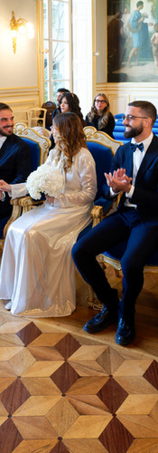 Photo couleur du mariage civil d’Annapaola et Angelo à la mairie du 7e arrondissement de Paris. Les mariés échangent un regard complice pendant que leurs invités applaudissent autour d’eux. La scène, baignée de lumière naturelle et mise en valeur par le décor doré et les peintures murales, témoigne d’une atmosphère joyeuse et élégante. Reportage réalisé par Colombe Photographie, photographe de mariage civil à Paris et en région parisienne.