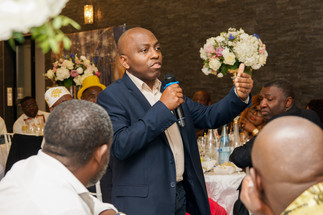Portrait d’un invité prenant la parole avec émotion pendant le repas organisé pour les 50 ans d’Armel. La scène se déroule dans une salle décorée avec des compositions florales, entourée d’invités attentifs. Photo capturée lors d’un événement privé en région parisienne par Colombe Photographie, photographe d’événements à Gentilly et dans toute l’Île-de-France.